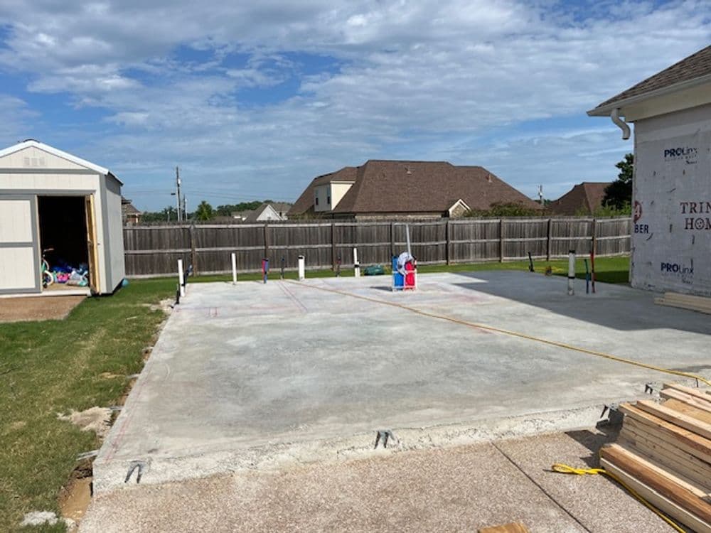 Construction site with a concrete slab and wooden materials, ready for building a new home.
