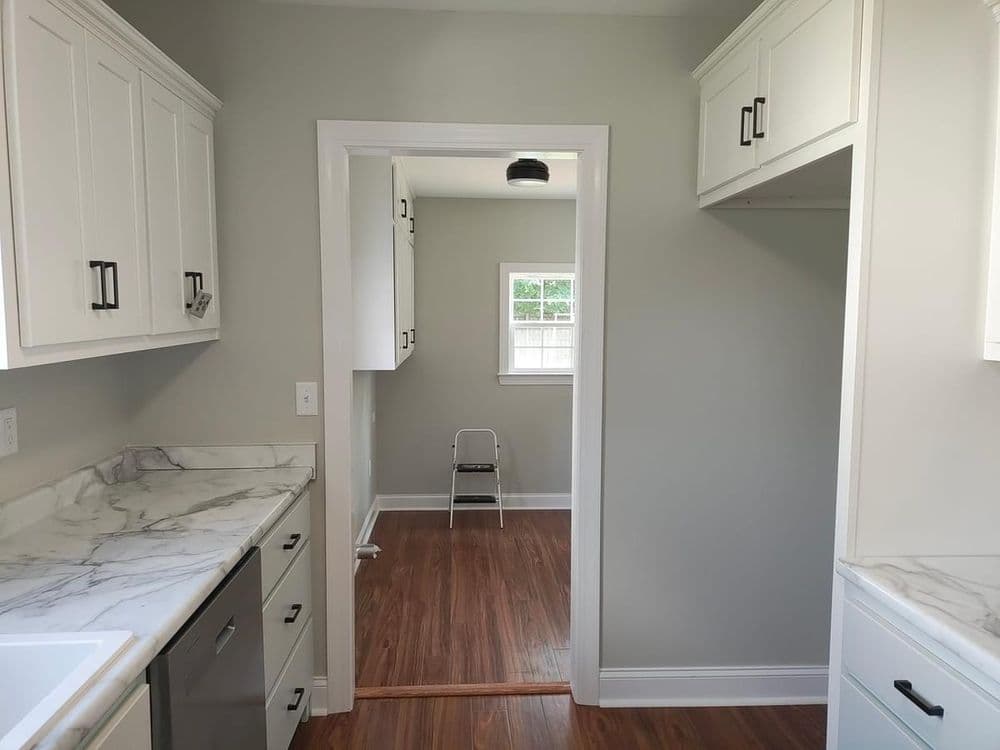 Modern kitchen with marble countertops, white cabinets, and a view of an adjoining room.