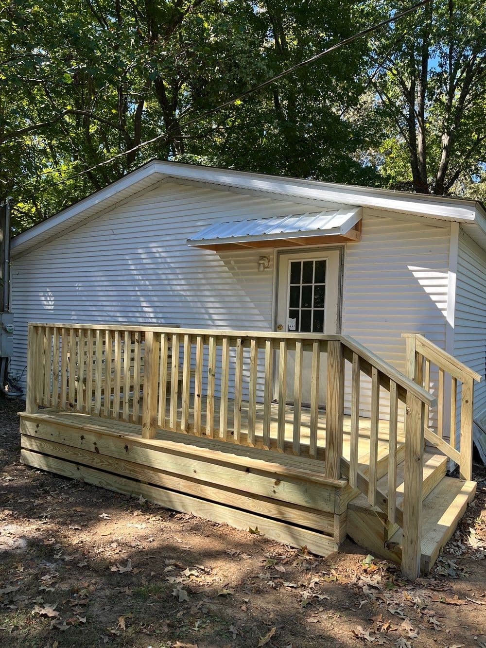 Newly built wooden deck leading to a white cabin surrounded by trees.
