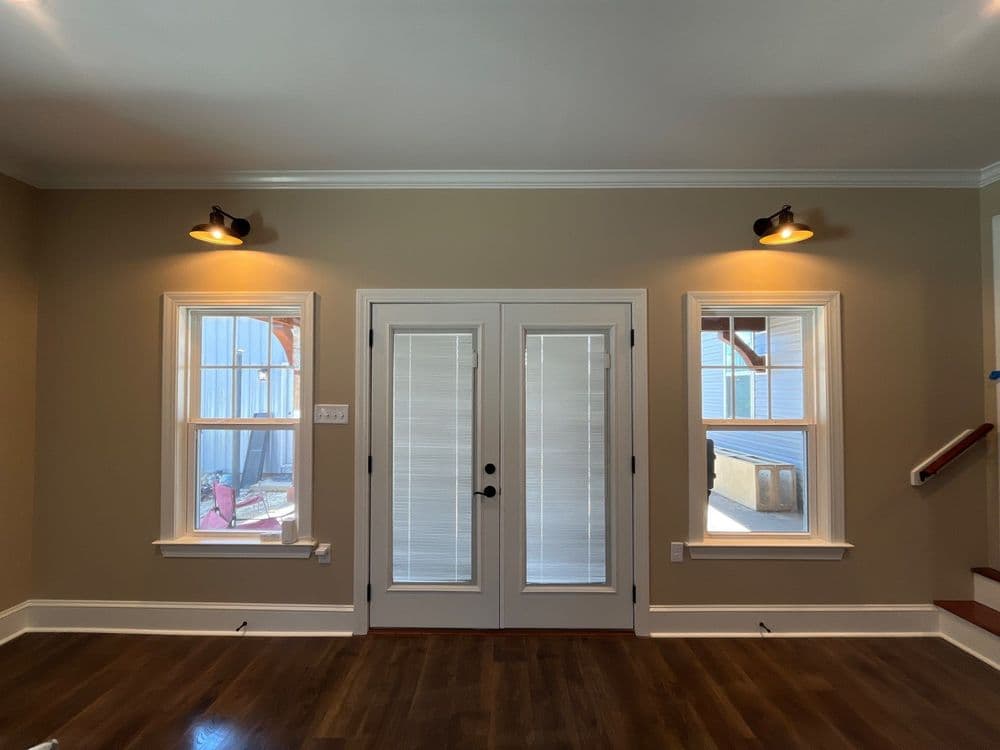 Modern interior room featuring double doors, wall sconces, and large windows. Elegant hardwood floor.