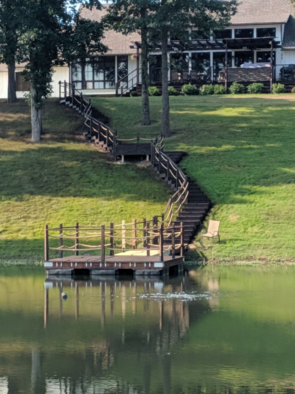 Wooden dock and stairs leading to a serene lake with a house in the background.