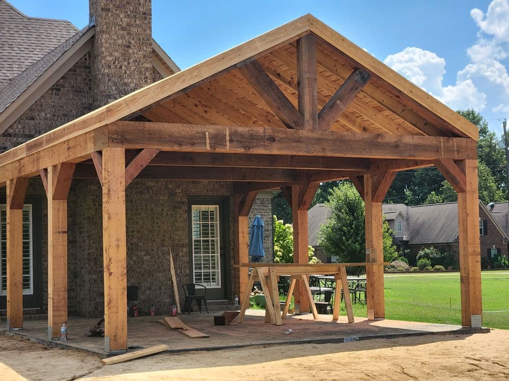 Newly built wooden porch with a gabled roof and rustic beams, overlooking a green lawn.