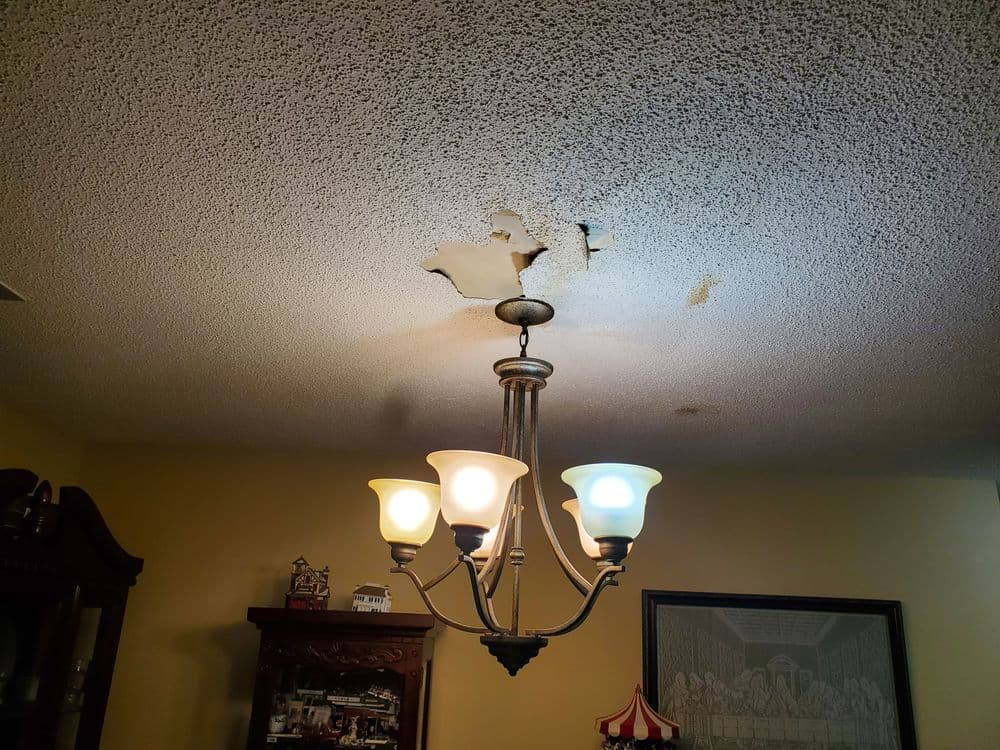 Ceiling damage with peeling paint above a chandelier in a living room.