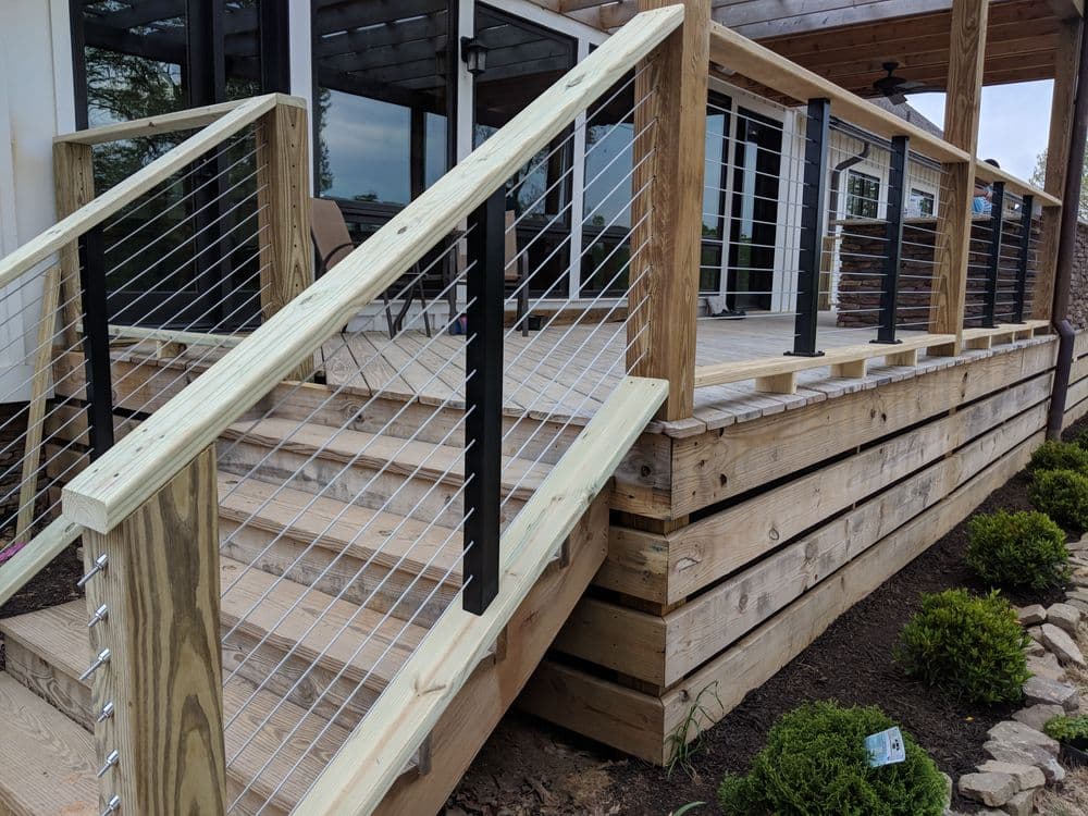 Modern wooden deck with cable railing and steps, surrounded by neatly trimmed greenery.