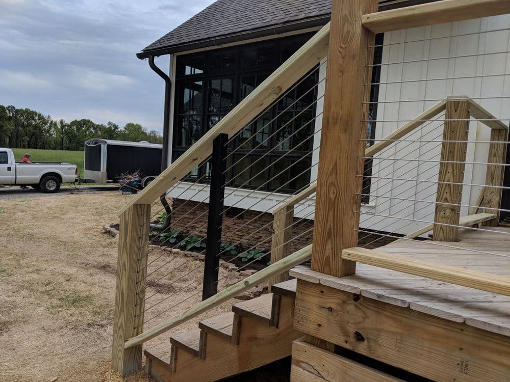 Wooden deck stairs with cable railings leading to a modern home exterior.