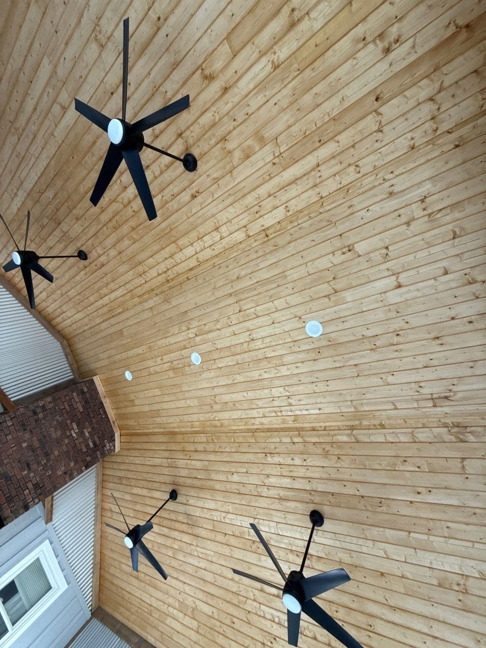 Ceiling with wooden panels and black ceiling fans in a modern outdoor space.