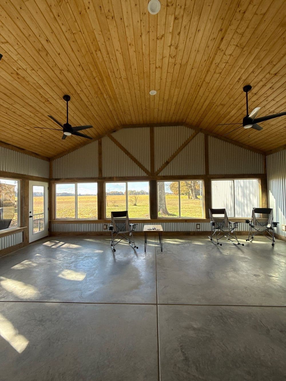 Spacious sunlit indoor space with wooden ceiling, large windows, and seating area.