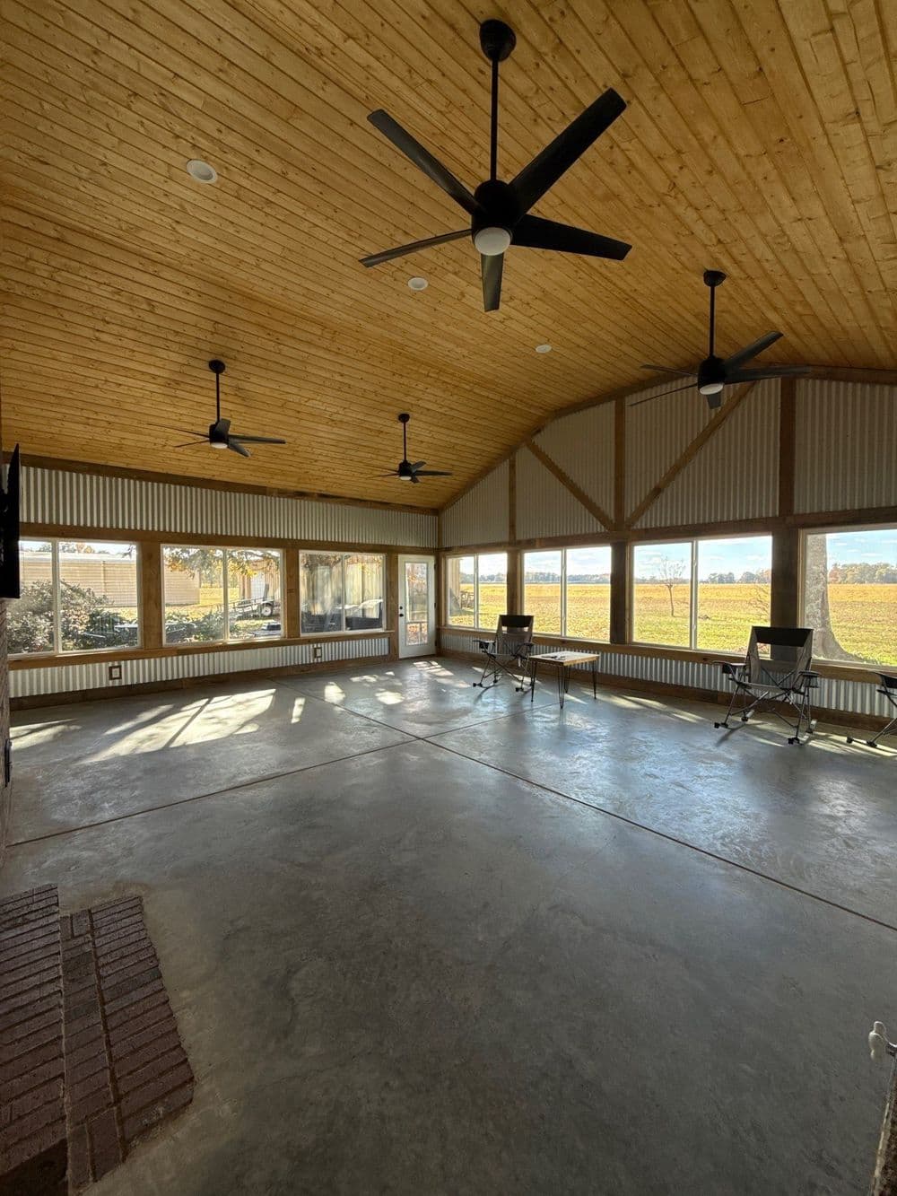 Spacious sunroom with wood ceiling, large windows, and concrete floor overlooking vineyard.