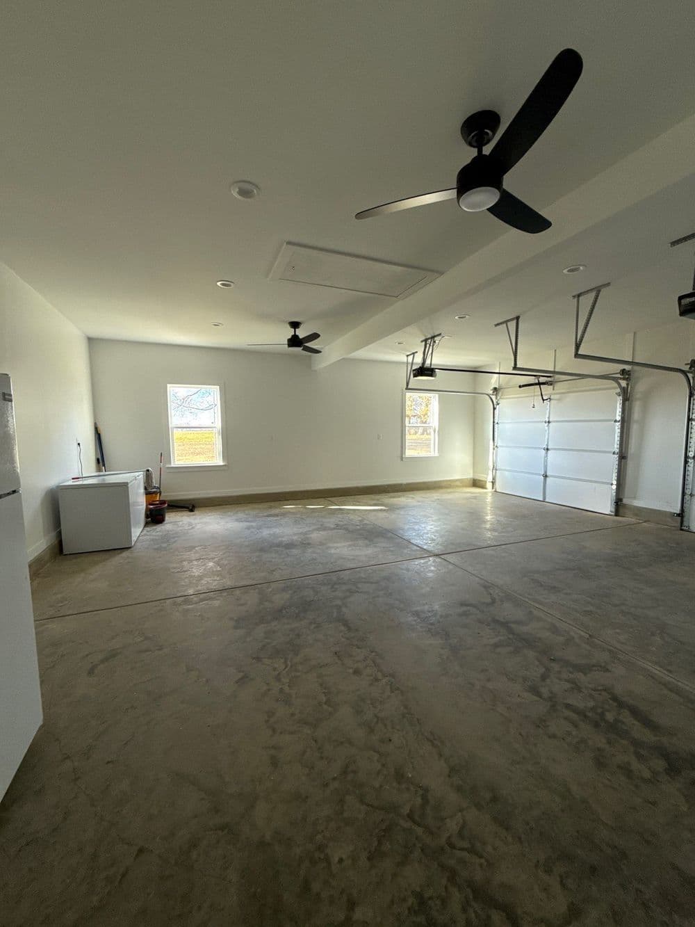 Spacious, well-lit garage with concrete floor, windows, fans, and garage door.