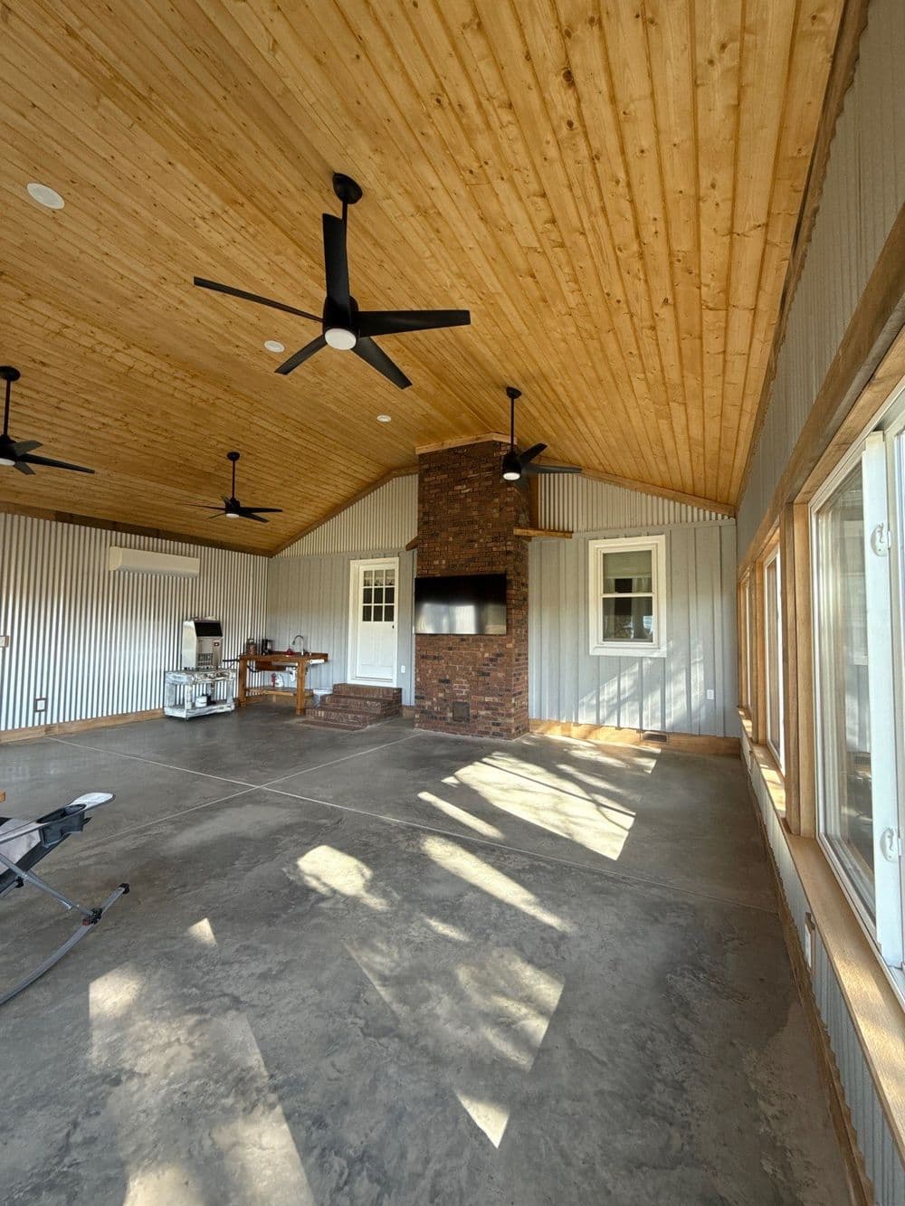 Rustic interior of a modern recreational space with wooden ceiling, stone fireplace, and fans.
